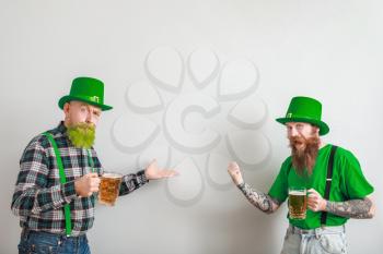 Bearded men with glasses of beer showing something on light background. St. Patrick's Day celebration�
