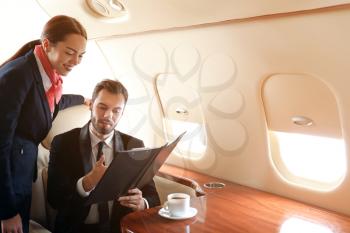 Air hostess showing menu to businessman on board the modern private airplane�
