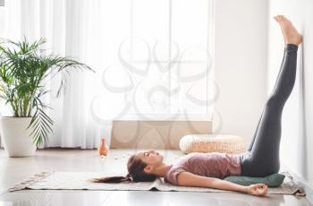 Beautiful young woman practicing yoga at home�