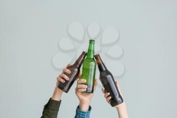 Hands clinking bottles of beer on grey background�