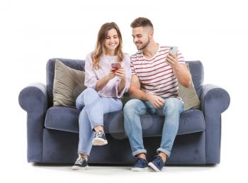 Young couple with mobile phones sitting on sofa against white background�