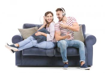 Young couple listening to music while sitting on sofa against white background�