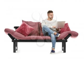 Young man with laptop sitting on sofa against white background�
