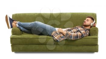Young man listening to music while lying on sofa against white background�