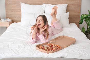 Morning of beautiful young woman eating tasty pizza in bedroom�