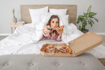 Morning of beautiful young woman eating tasty pizza while watching TV in bedroom�