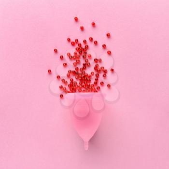Menstrual cup with red beads on color background�