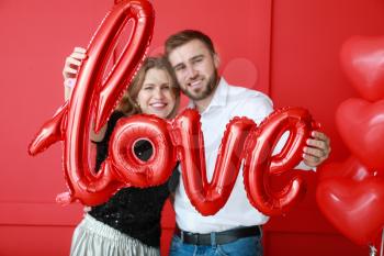 Happy young couple with balloon in shape of word LOVE on color background. Valentine's Day celebration�