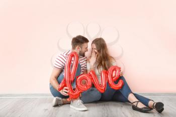 Happy young couple with balloon in shape of word LOVE sitting near color wall. Valentine's Day celebration�
