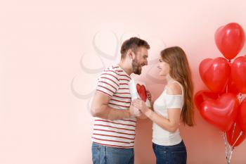 Happy young couple with gift on color background. Valentine's Day celebration�