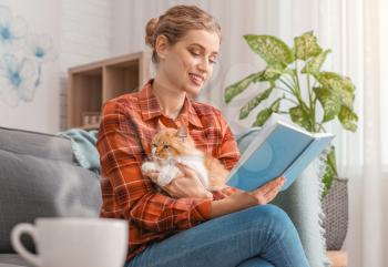 Beautiful young woman with cute cat reading book at home�