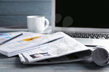 Newspapers, laptop and cup of coffee on table�