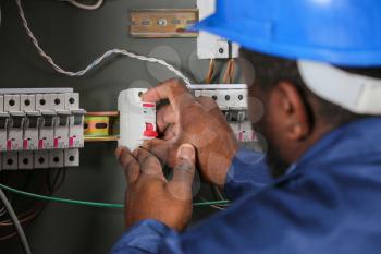African-American electrician performing wiring in distribution board�
