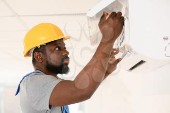 African-American electrician repairing air conditioner indoors�