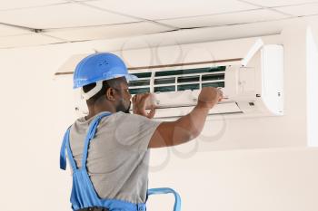 African-American electrician repairing air conditioner indoors�