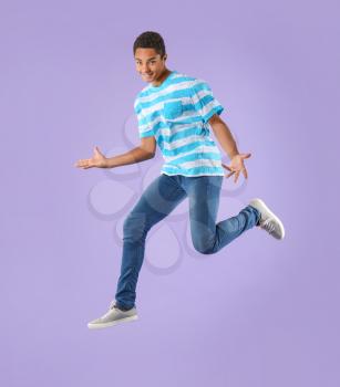 Jumping African-American teenager boy on color background�
