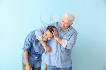 Young man and his father having fun on color background�