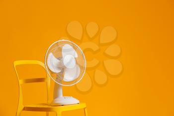 Electric fan on chair against color background�