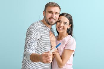 Happy young couple with pregnancy test on color background�