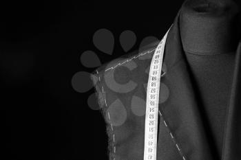 Tailor's mannequin with unfinished clothes and measuring tape on dark background, closeup�
