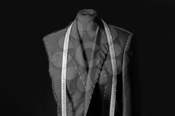 Tailor's mannequin with unfinished clothes and measuring tape on dark background�