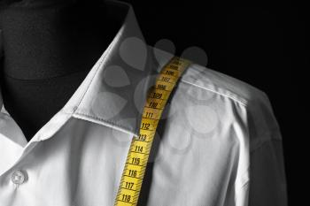 Mannequin with custom tailored shirt and measuring tape on dark background, closeup�