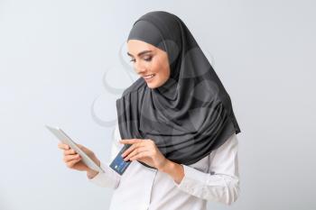 Beautiful Arab woman with tablet computer and credit card on light background�