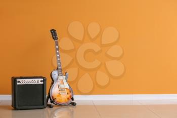 Modern guitar and amplifier near color wall 