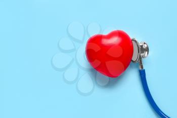Modern stethoscope and red heart on color background�