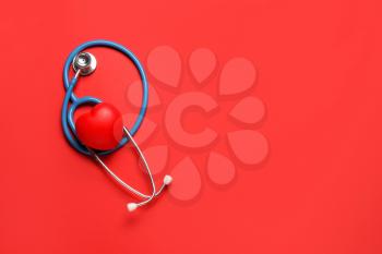 Modern stethoscope and red heart on color background�