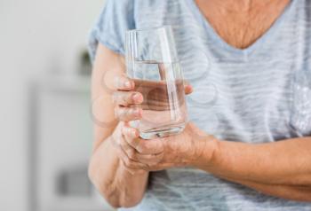 Senior woman suffering from Parkinson syndrome with glass of water in clinic, closeup�