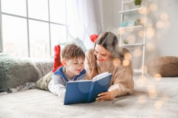 Cute little boy with mother reading book at home�