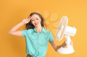 Young woman with electric fan on color background�