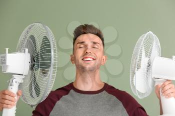 Young man with electric fans on color background�