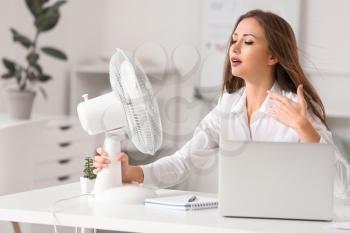 Young woman using electric fan during heatwave in office�