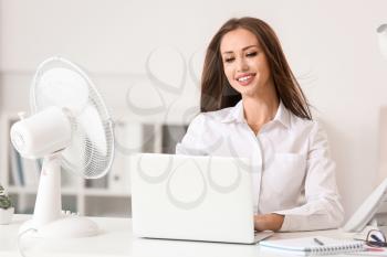 Young woman using electric fan during heatwave in office�