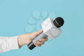 Journalist's hand with microphone on color background�