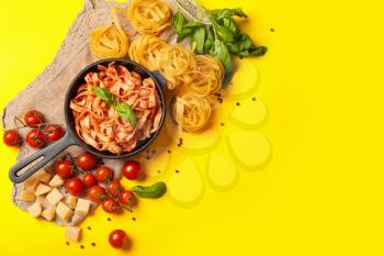 Frying pan with boiled, raw pasta and tomato sauce on color background�