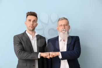 Portrait of senior man and his adult son bumping fists on color background�