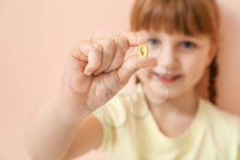 Little girl with fish oil pill on color background, closeup�