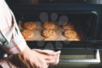 Woman taking baking tray with cookies out of oven�