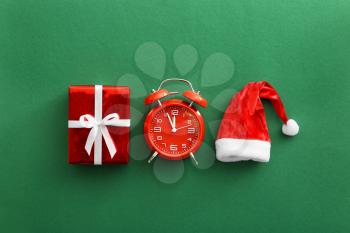 Alarm clock with Christmas gift and Santa Claus hat on color background�