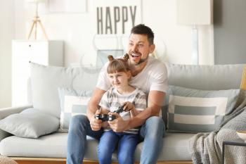 Father and his little daughter playing video games at home�