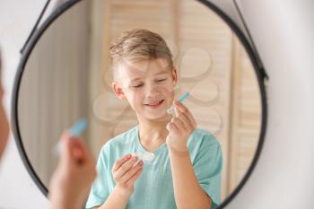 Little boy with contact lens case and tweezers near mirror at home�