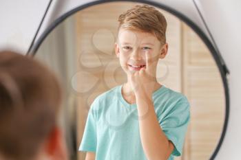Little boy putting in contact lens near mirror at home�