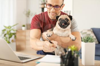 Handsome man with cute pug dog and laptop at home�