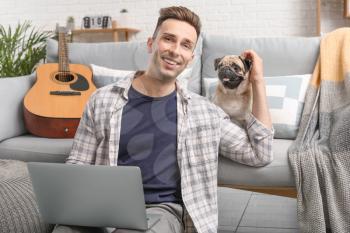 Handsome man with laptop and cute pug dog at home�