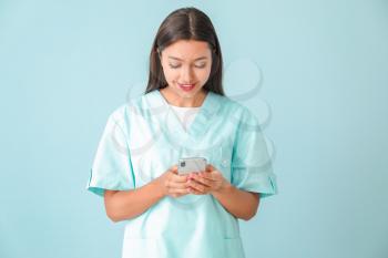 Young nurse with mobile phone on color background�