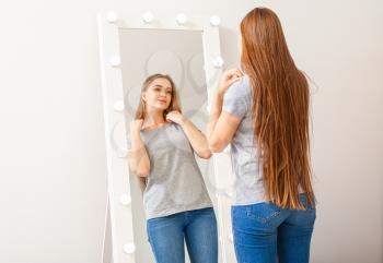 Beautiful young woman looking at her reflection in mirror�