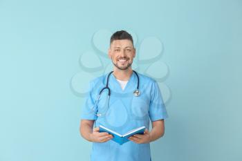 Male cardiologist with book on color background�